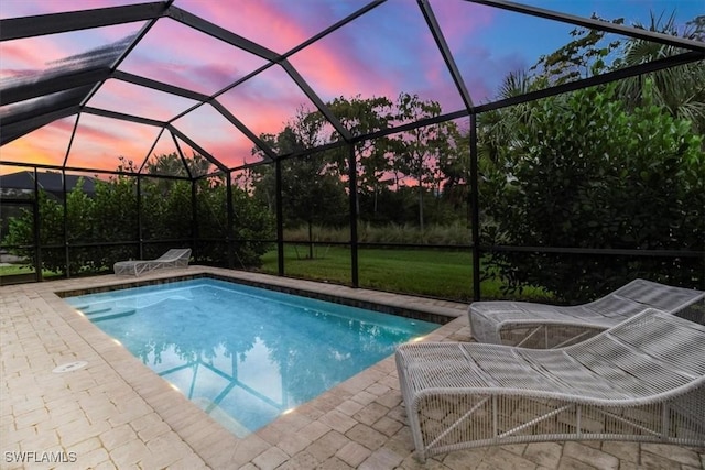 pool at dusk with glass enclosure and a patio area