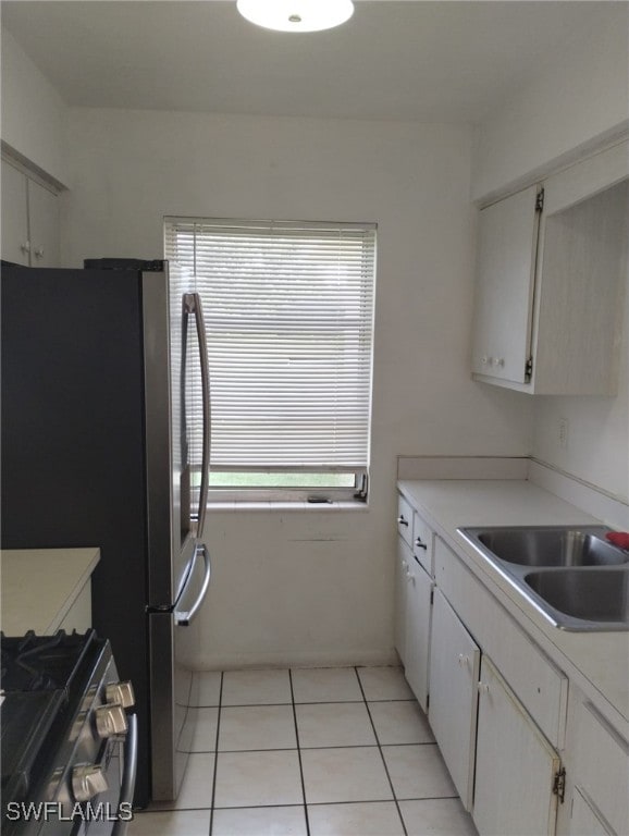 kitchen with light tile patterned floors, sink, gas stove, and white cabinetry