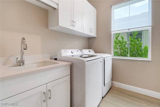 laundry area featuring cabinets, sink, washer and dryer, and light hardwood / wood-style flooring