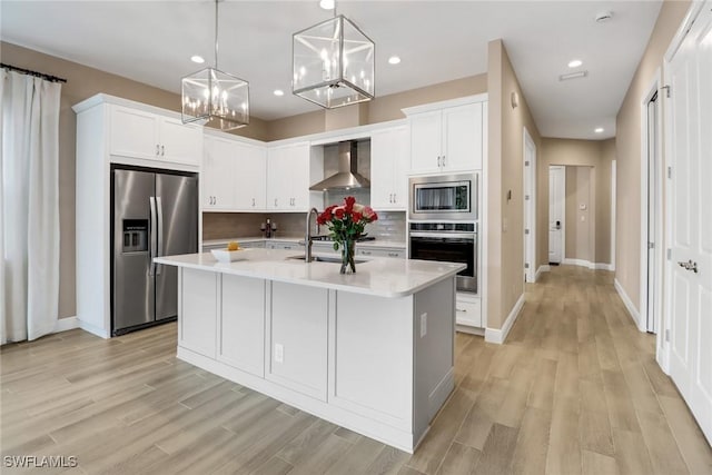 kitchen with wall chimney exhaust hood, sink, appliances with stainless steel finishes, and an island with sink