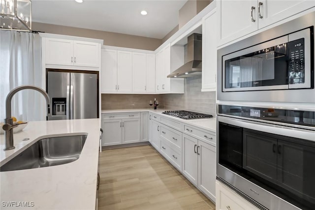 kitchen featuring appliances with stainless steel finishes, tasteful backsplash, wall chimney exhaust hood, sink, and white cabinets