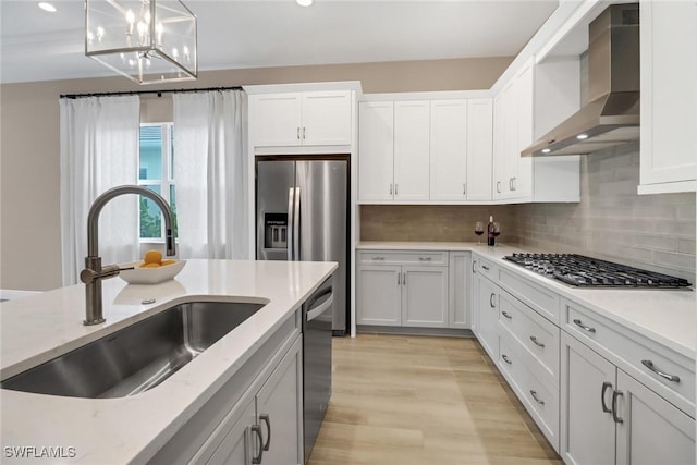 kitchen featuring sink, white cabinets, hanging light fixtures, and wall chimney range hood