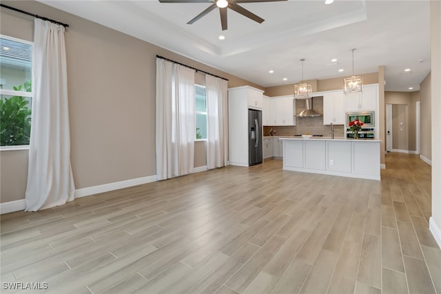 kitchen featuring white cabinets, decorative light fixtures, a kitchen island, and wall chimney range hood