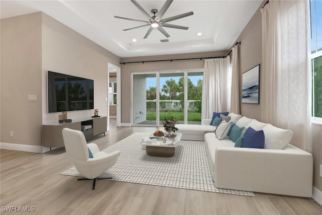 living room featuring light wood-type flooring, a tray ceiling, and ceiling fan