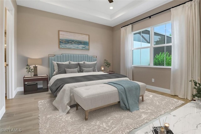 bedroom featuring a tray ceiling, ceiling fan, and light hardwood / wood-style floors