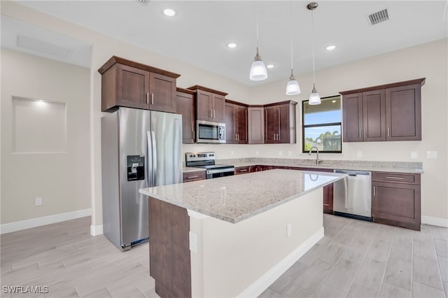 kitchen with appliances with stainless steel finishes, sink, light stone counters, pendant lighting, and a center island