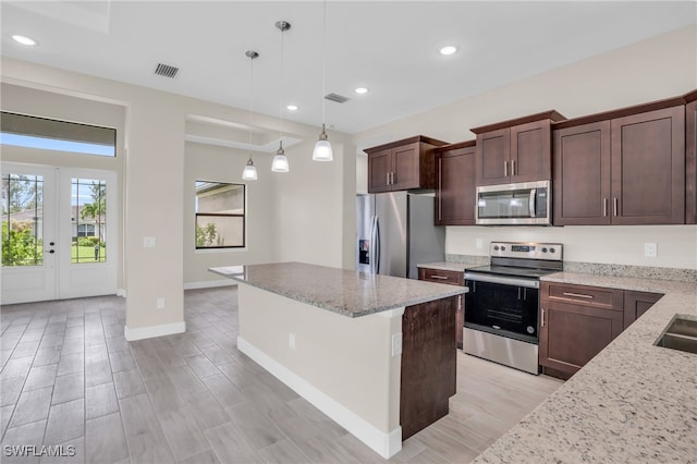 kitchen featuring hanging light fixtures, dark brown cabinetry, light stone countertops, a kitchen island, and stainless steel appliances