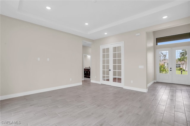 spare room with light hardwood / wood-style floors, french doors, and a tray ceiling