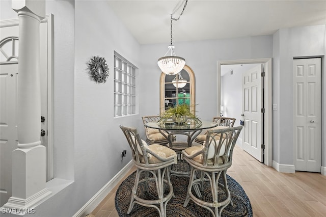 dining area featuring a notable chandelier, light hardwood / wood-style floors, and ornate columns