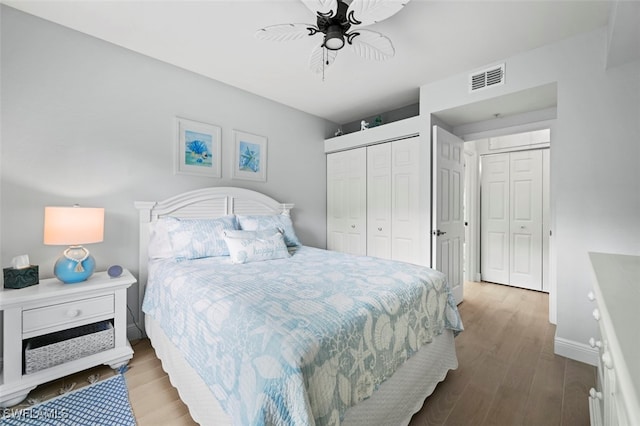 bedroom featuring ceiling fan, multiple closets, and light hardwood / wood-style flooring