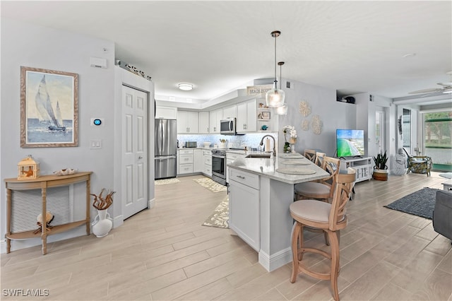 kitchen featuring pendant lighting, tasteful backsplash, white cabinetry, light stone counters, and stainless steel appliances