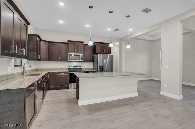 kitchen featuring sink, decorative light fixtures, appliances with stainless steel finishes, light hardwood / wood-style flooring, and a kitchen island