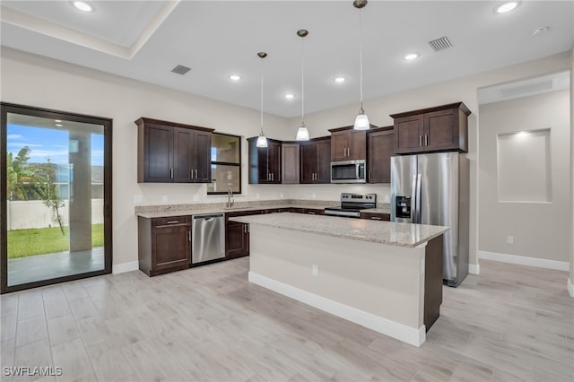 kitchen featuring pendant lighting, a kitchen island, appliances with stainless steel finishes, light stone counters, and sink