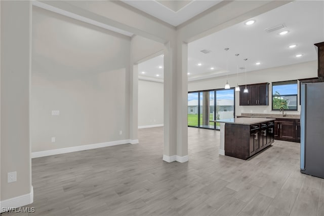 kitchen featuring dark brown cabinetry, pendant lighting, a kitchen island, light hardwood / wood-style floors, and stainless steel fridge