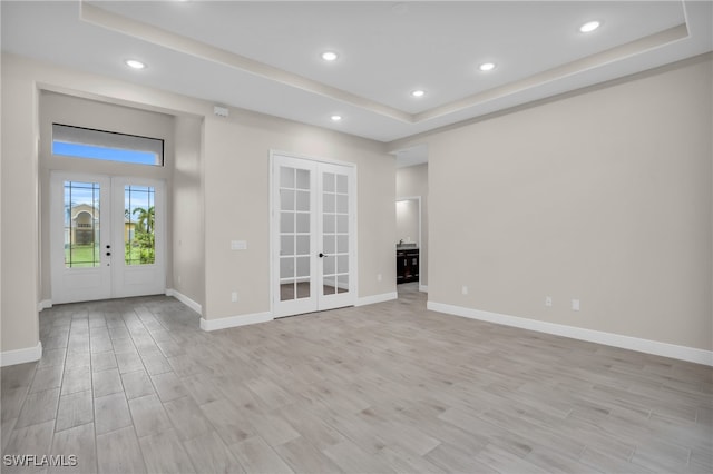 spare room with a raised ceiling, french doors, and light hardwood / wood-style floors