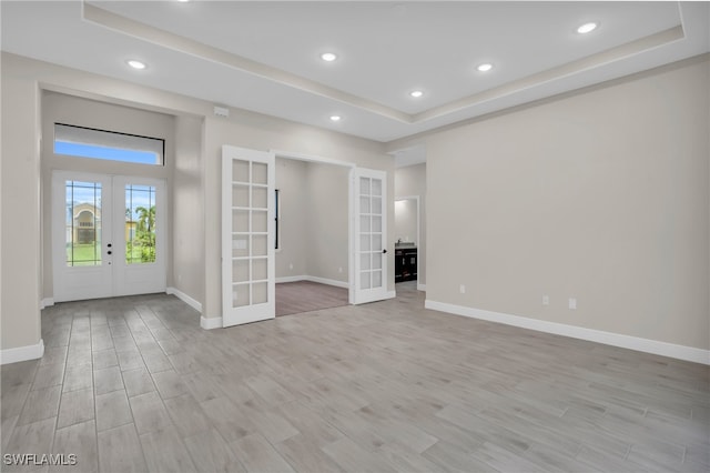 spare room featuring light hardwood / wood-style flooring, a raised ceiling, and french doors