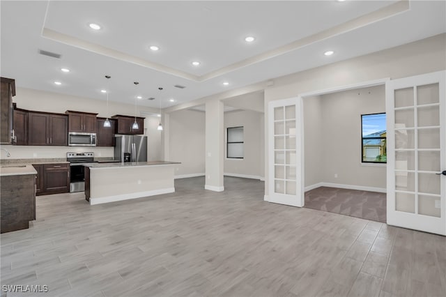 kitchen featuring a raised ceiling, dark brown cabinetry, french doors, a center island, and stainless steel appliances