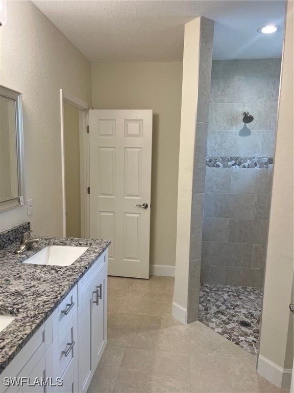 bathroom featuring tile patterned flooring, a tile shower, and vanity