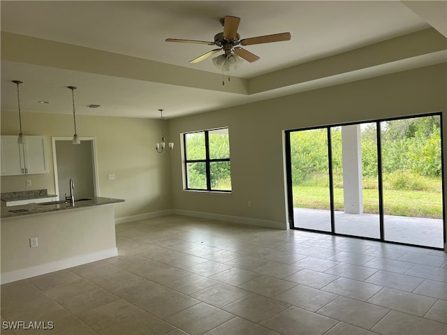 interior space with sink, a tray ceiling, ceiling fan with notable chandelier, and light tile patterned floors