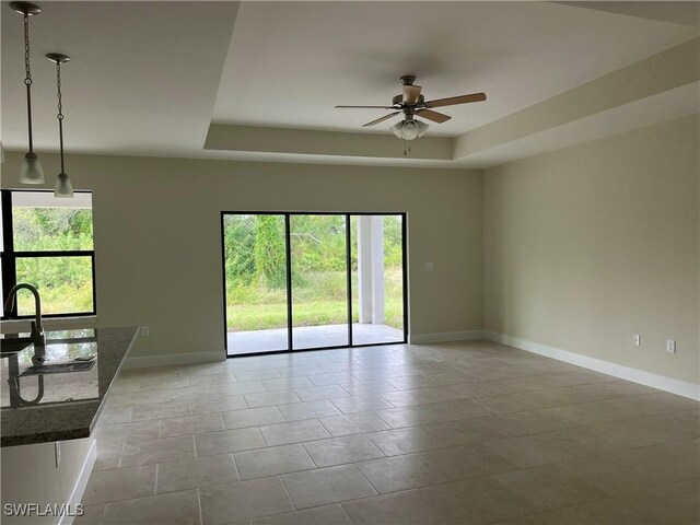 spare room with light tile patterned floors, a raised ceiling, plenty of natural light, and ceiling fan