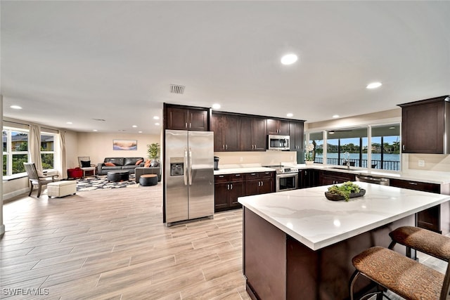 kitchen with appliances with stainless steel finishes, plenty of natural light, a kitchen breakfast bar, and dark brown cabinets