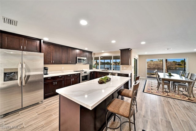 kitchen featuring appliances with stainless steel finishes, plenty of natural light, a kitchen breakfast bar, and light hardwood / wood-style flooring