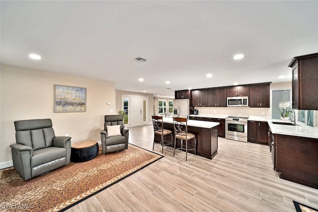 kitchen featuring dark brown cabinetry, a kitchen island, appliances with stainless steel finishes, light hardwood / wood-style floors, and a breakfast bar area