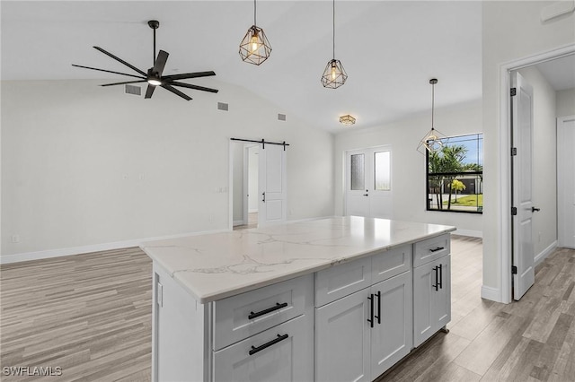 kitchen with pendant lighting, white cabinetry, a barn door, a center island, and light stone countertops