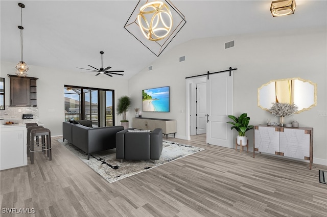 living room with ceiling fan with notable chandelier, light hardwood / wood-style flooring, high vaulted ceiling, and a barn door