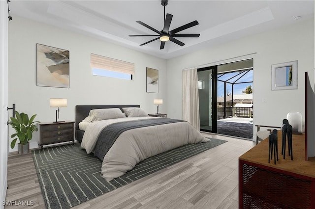 bedroom with ceiling fan, wood-type flooring, access to exterior, and a raised ceiling