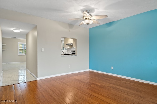 spare room with light wood-type flooring, a ceiling fan, baseboards, and a textured ceiling