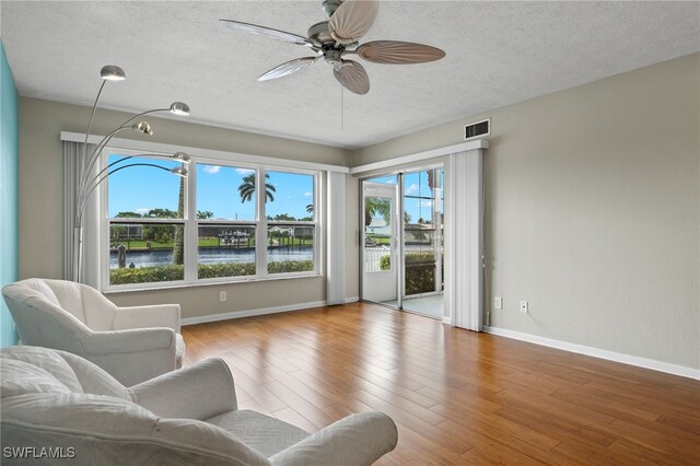 living room featuring ceiling fan, a textured ceiling, hardwood / wood-style floors, and a water view