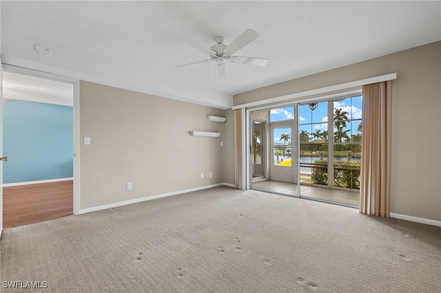 empty room featuring light carpet, a water view, ceiling fan, and baseboards