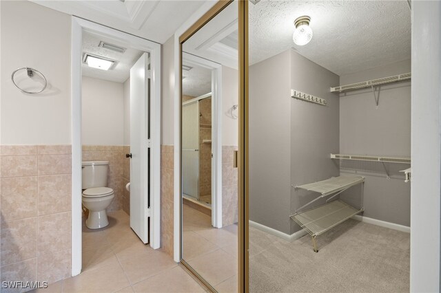 bathroom with toilet, a textured ceiling, tile patterned flooring, and tile walls