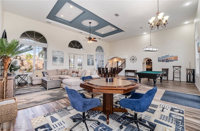 dining area featuring light hardwood / wood-style floors, a raised ceiling, a towering ceiling, and ceiling fan with notable chandelier