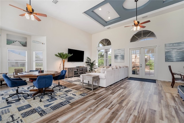 living room featuring a towering ceiling, ceiling fan, hardwood / wood-style flooring, and french doors