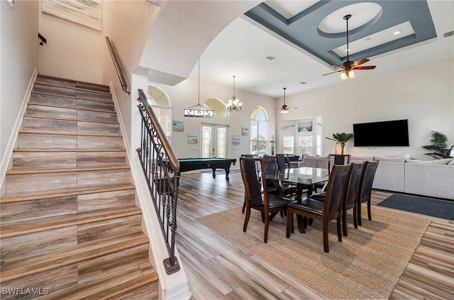 dining room featuring billiards, ceiling fan with notable chandelier, a tray ceiling, french doors, and hardwood / wood-style flooring