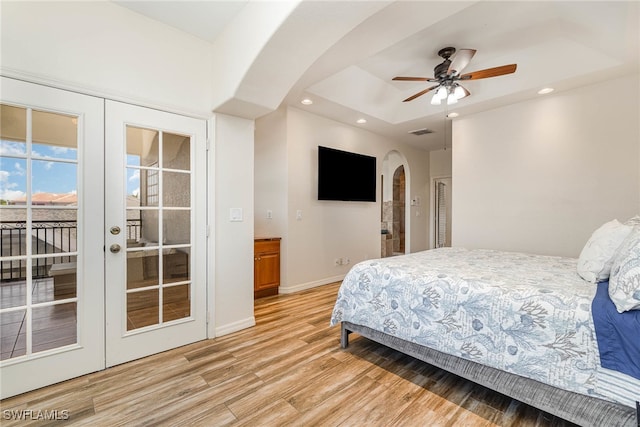 bedroom with access to outside, light hardwood / wood-style flooring, french doors, and a tray ceiling