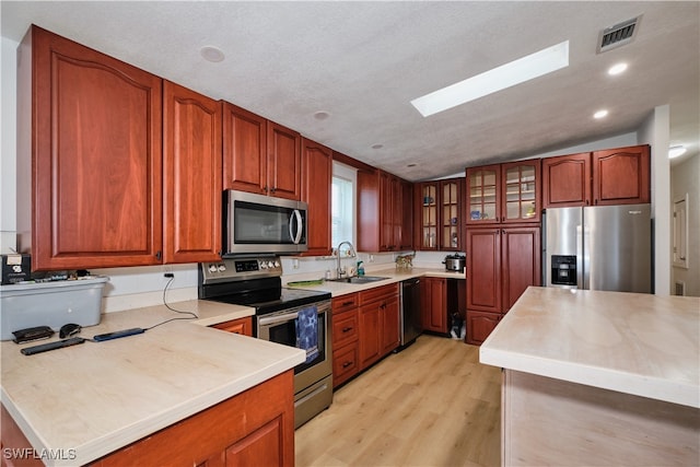 kitchen featuring appliances with stainless steel finishes, light hardwood / wood-style floors, sink, lofted ceiling with skylight, and a textured ceiling