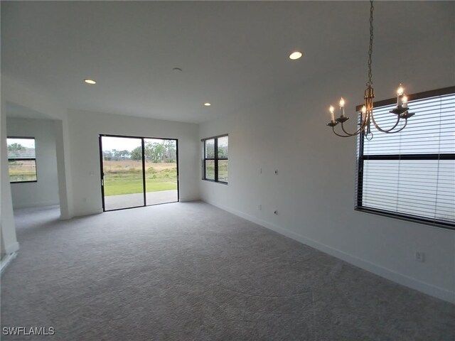 carpeted empty room with an inviting chandelier