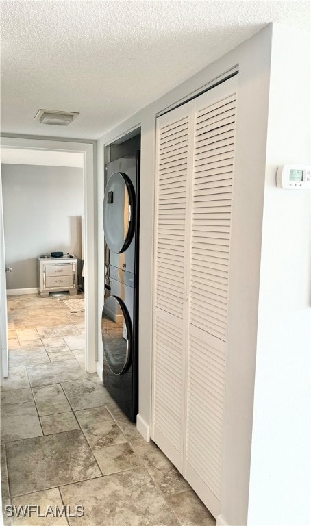 corridor with light tile patterned flooring, a textured ceiling, and stacked washer and clothes dryer