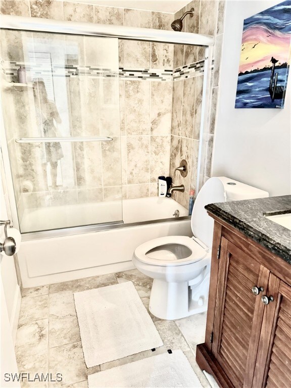 full bathroom with combined bath / shower with glass door, toilet, vanity, and tile patterned floors