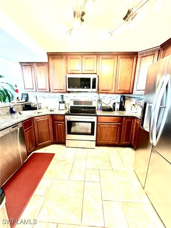 kitchen featuring appliances with stainless steel finishes, rail lighting, sink, light stone counters, and light tile patterned flooring