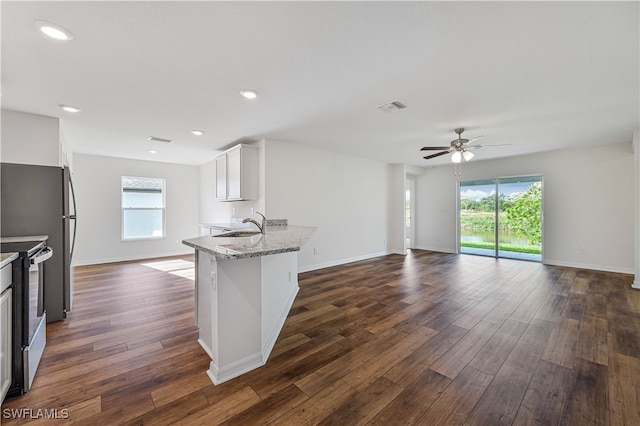 kitchen with dark wood-type flooring, stainless steel range oven, light stone counters, a healthy amount of sunlight, and white cabinetry