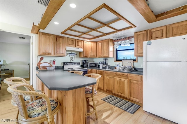 kitchen featuring kitchen peninsula, light wood-type flooring, a kitchen breakfast bar, and white appliances