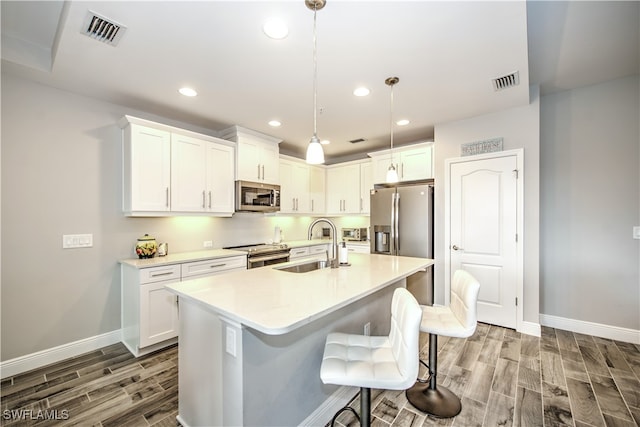 kitchen featuring appliances with stainless steel finishes, a kitchen bar, pendant lighting, hardwood / wood-style floors, and white cabinets