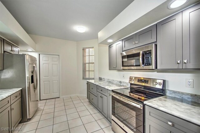 kitchen featuring gray cabinetry, light tile patterned flooring, light stone countertops, and stainless steel appliances