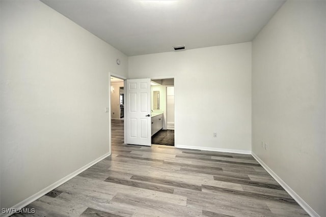 unfurnished bedroom featuring light wood finished floors, ensuite bath, visible vents, and baseboards