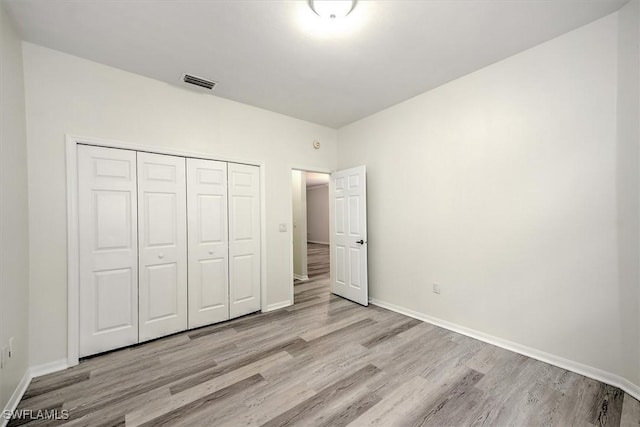 unfurnished bedroom with light wood-type flooring, baseboards, visible vents, and a closet