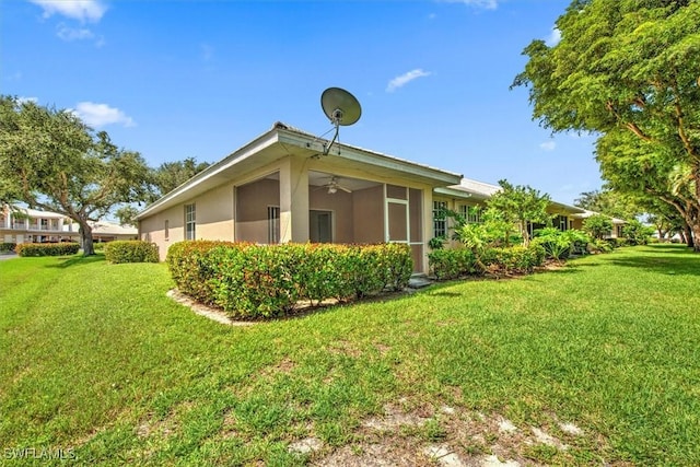 view of side of home with ceiling fan, a yard, and stucco siding